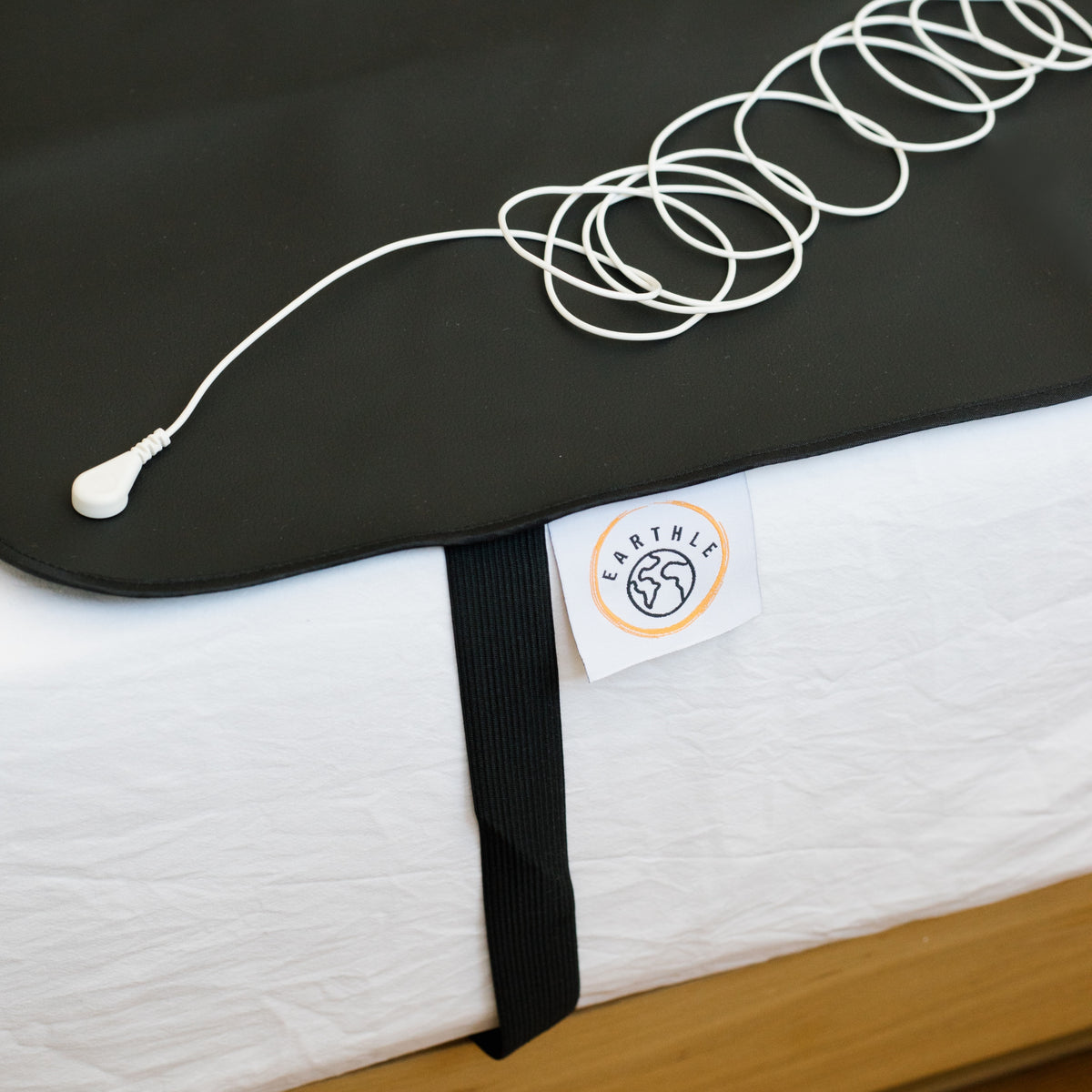 Earthing cable coiled on the black sleeping mat on a made bed