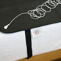 Earthing cable coiled on the black sleeping mat on a made bed