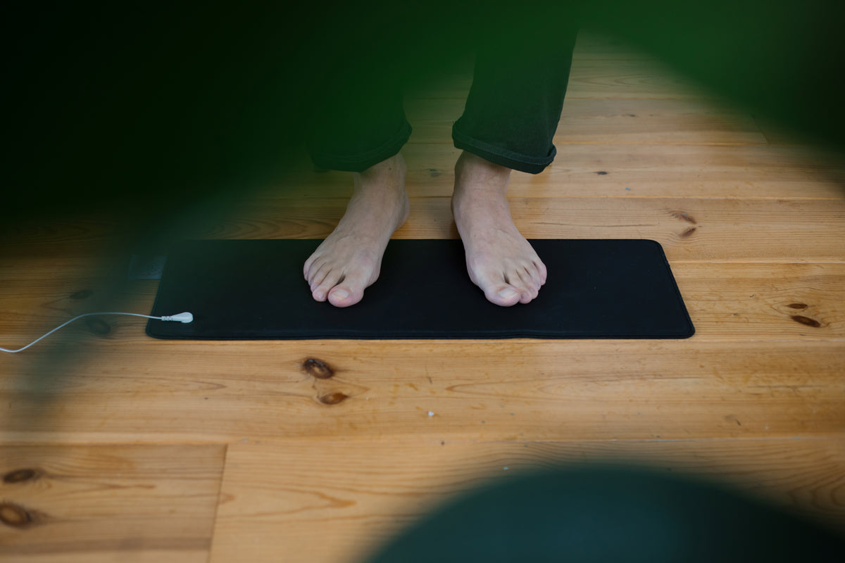 Bare feet on the Earthle earthing mat on the floor, used as a foot mat