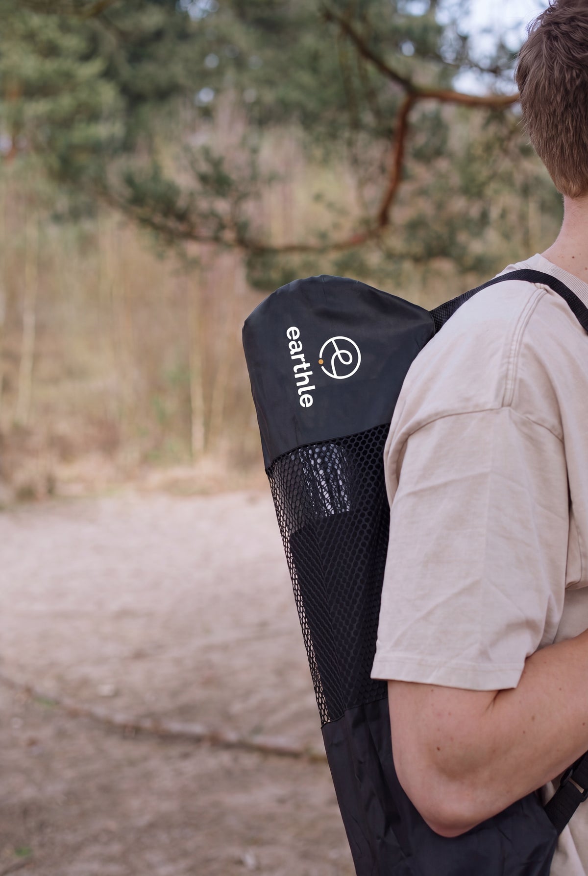 Someone carrying the Earthle earthing yoga mat in its bag on their back, outdoors in the forest