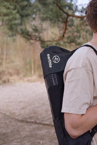 Someone carrying the Earthle earthing yoga mat in its bag on their back, outdoors in the forest