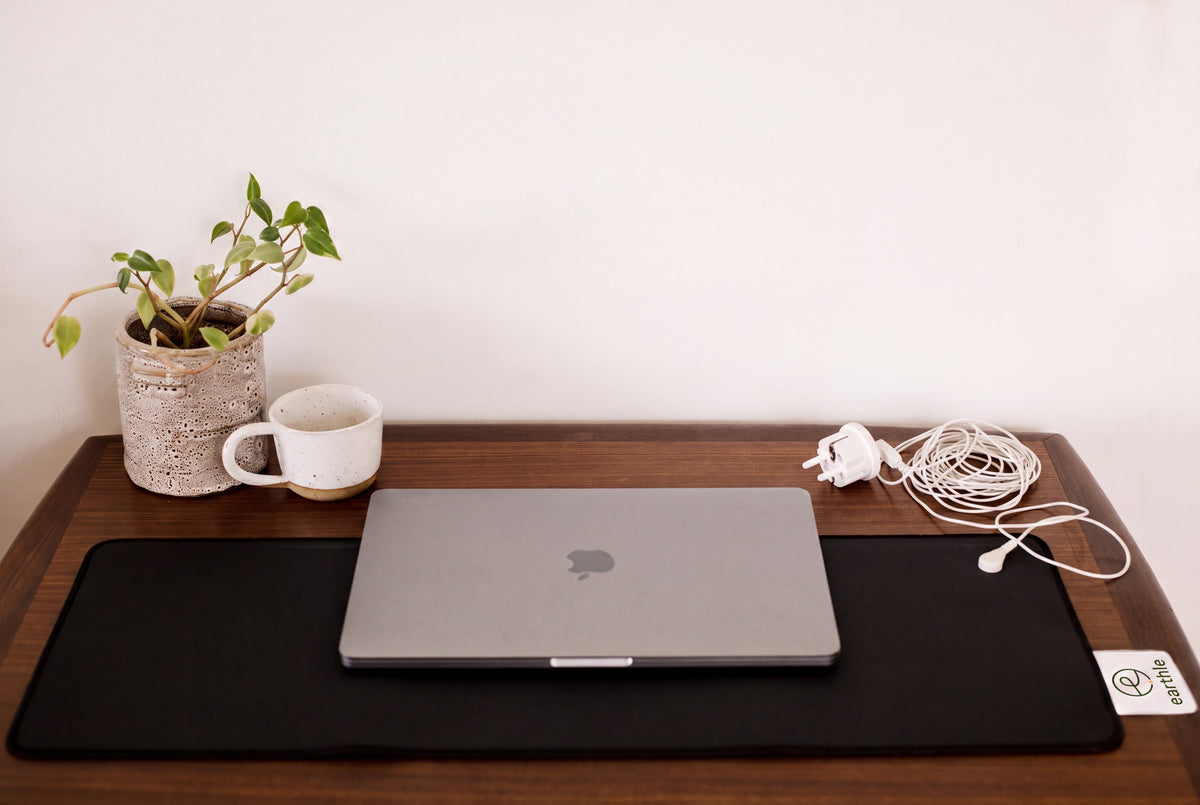 Earthle earthing desk mat on a desk with laptop, plant and mug, cable running to the socket