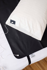 Earthle earthing pillowcase on a bed next to the black earthing sleeping mat, with the earthing cable attached